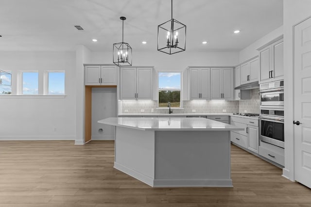 kitchen with pendant lighting, a kitchen island, light wood-type flooring, and backsplash