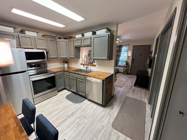 kitchen featuring appliances with stainless steel finishes, tasteful backsplash, sink, butcher block counters, and light wood-type flooring