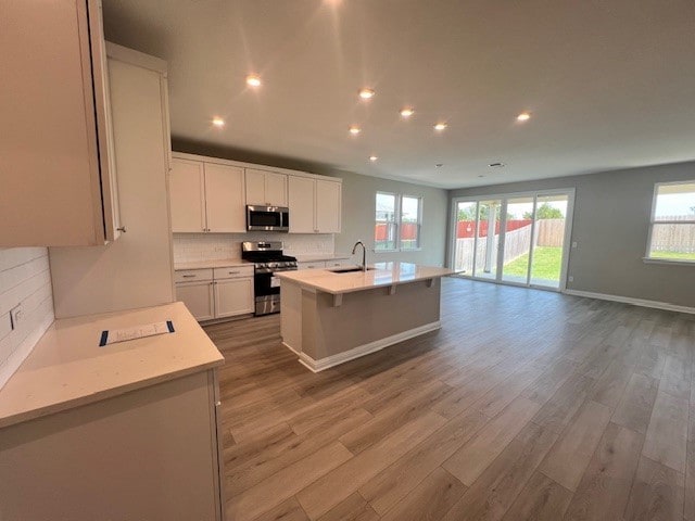 kitchen with appliances with stainless steel finishes, sink, white cabinets, decorative backsplash, and a center island with sink