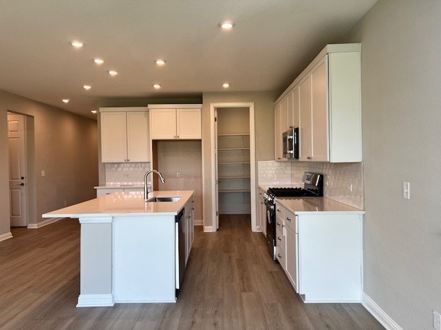 kitchen with sink, a center island with sink, dark hardwood / wood-style floors, stainless steel appliances, and white cabinets