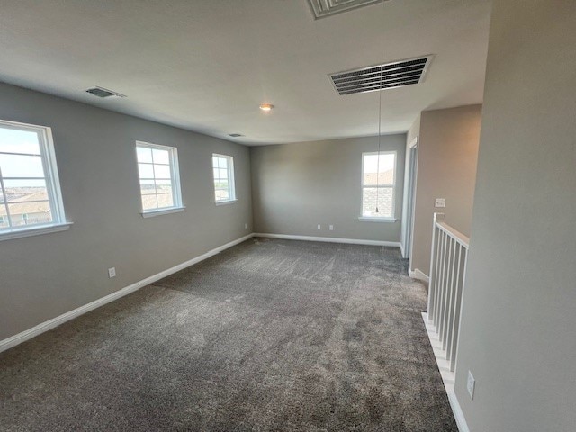 unfurnished room featuring a wealth of natural light and dark colored carpet