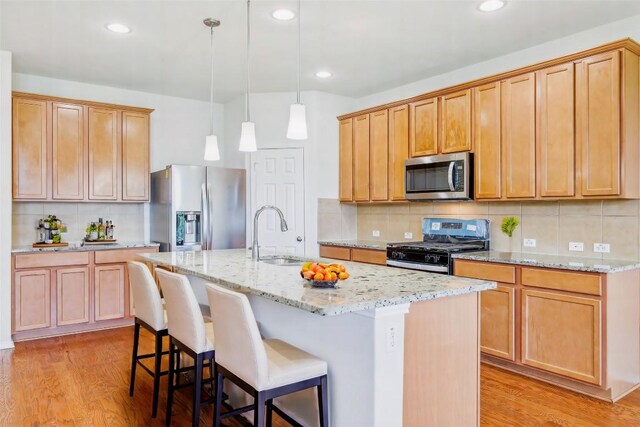 kitchen with backsplash, stainless steel appliances, light hardwood / wood-style flooring, and a kitchen island with sink