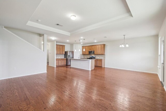 unfurnished living room featuring hardwood / wood-style floors, sink, a raised ceiling, and an inviting chandelier