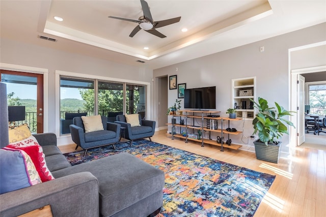 living room with light hardwood / wood-style floors, ceiling fan, and a tray ceiling