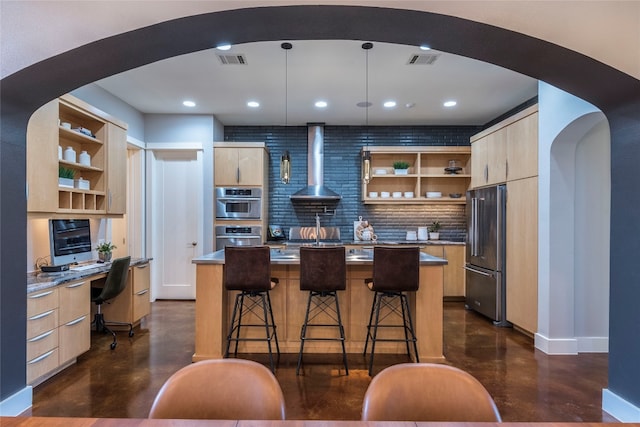 kitchen featuring appliances with stainless steel finishes, backsplash, a center island, and wall chimney range hood