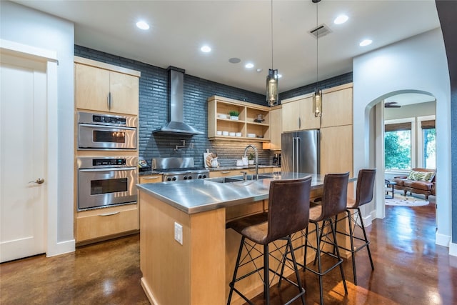 kitchen with tasteful backsplash, wall chimney range hood, stainless steel appliances, pendant lighting, and stainless steel counters