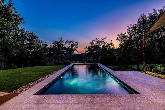 pool at dusk featuring a yard