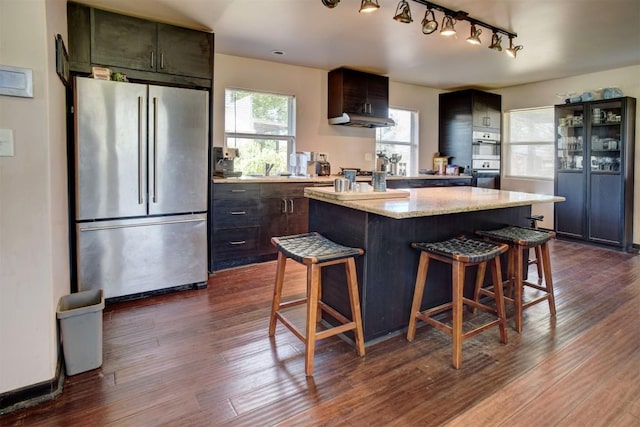 128 Gonzales St, Paige, TX 78659 - kitchen with dark wood-style floors, a kitchen island, a breakfast bar, and freestanding refrigerator