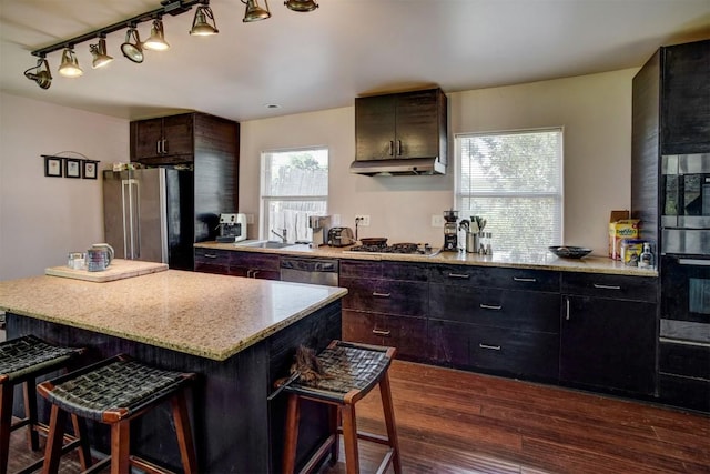 128 Gonzales St, Paige, TX 78659 - kitchen with a kitchen bar, dark wood finished floors, appliances with stainless steel finishes, under cabinet range hood, and a center island