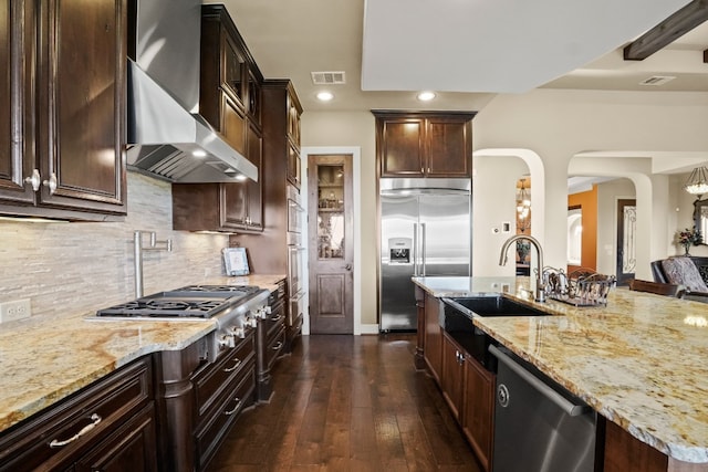 kitchen with dark hardwood / wood-style flooring, wall chimney exhaust hood, sink, light stone countertops, and appliances with stainless steel finishes