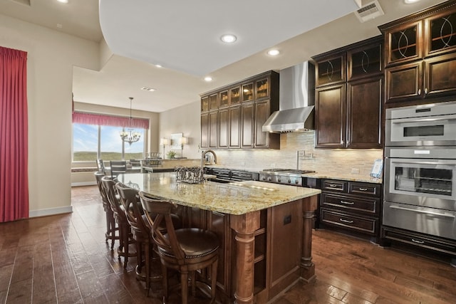 kitchen featuring tasteful backsplash, stainless steel appliances, wall chimney range hood, decorative light fixtures, and dark hardwood / wood-style floors