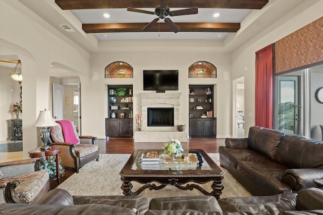 living room featuring ceiling fan, built in shelves, beamed ceiling, a towering ceiling, and dark wood-type flooring