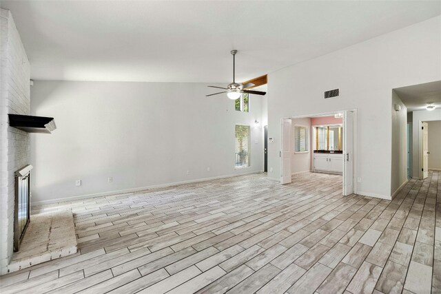 unfurnished living room with high vaulted ceiling, light wood-type flooring, ceiling fan, and a fireplace