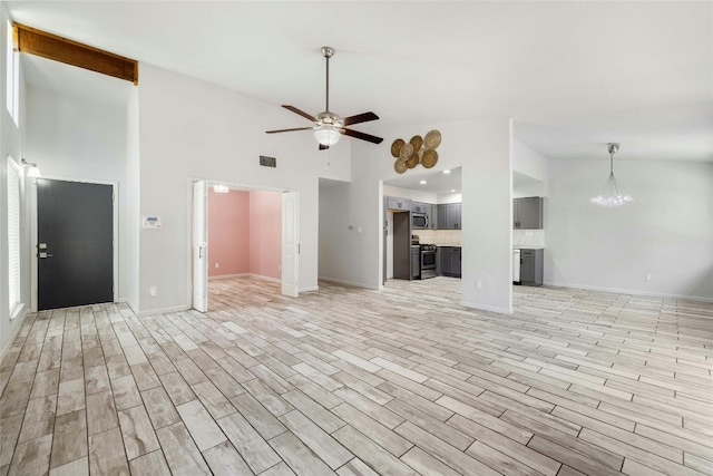 unfurnished living room featuring light hardwood / wood-style floors, a towering ceiling, and ceiling fan