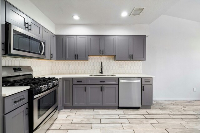 kitchen featuring appliances with stainless steel finishes, gray cabinetry, decorative backsplash, and sink