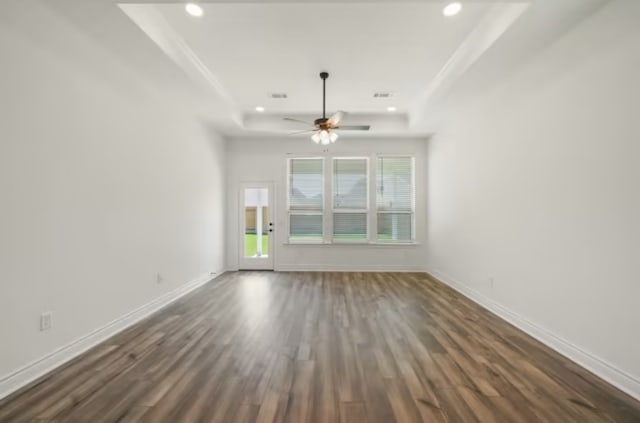 empty room featuring a raised ceiling, a healthy amount of sunlight, ceiling fan, and dark hardwood / wood-style floors