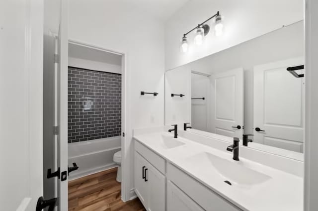 full bathroom with dual vanity, tiled shower / bath, wood-type flooring, and toilet