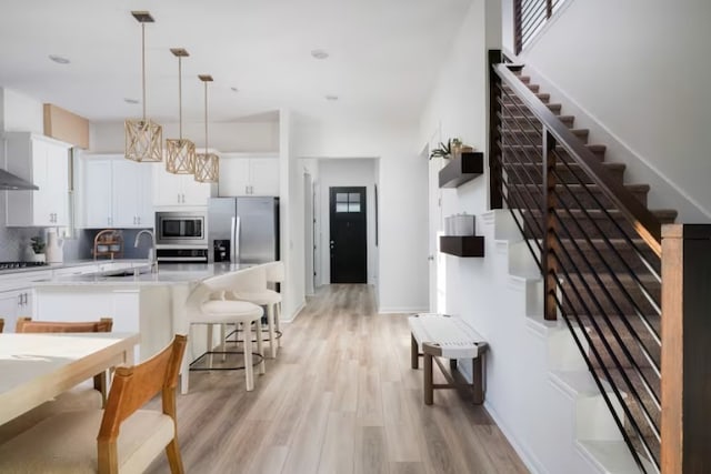 kitchen featuring stainless steel appliances, hanging light fixtures, white cabinets, sink, and light hardwood / wood-style flooring