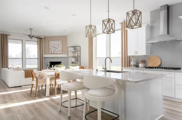 kitchen featuring tasteful backsplash, wall chimney exhaust hood, sink, light stone counters, and light hardwood / wood-style flooring