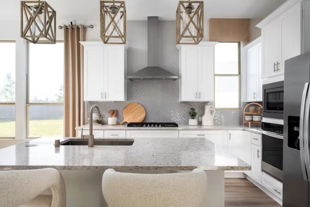 kitchen with tasteful backsplash, stainless steel appliances, wall chimney range hood, light stone counters, and wood-type flooring