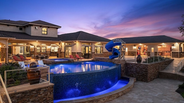 pool at dusk featuring a patio, an in ground hot tub, and pool water feature