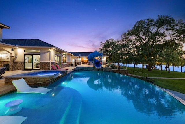 pool at dusk featuring a water slide, a yard, an in ground hot tub, and a patio area