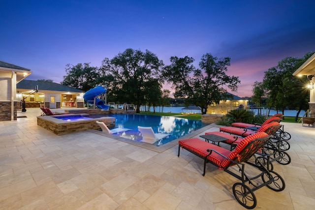 pool at dusk featuring an in ground hot tub and a patio