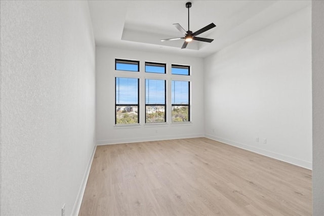 unfurnished room with light wood-type flooring, a raised ceiling, and ceiling fan