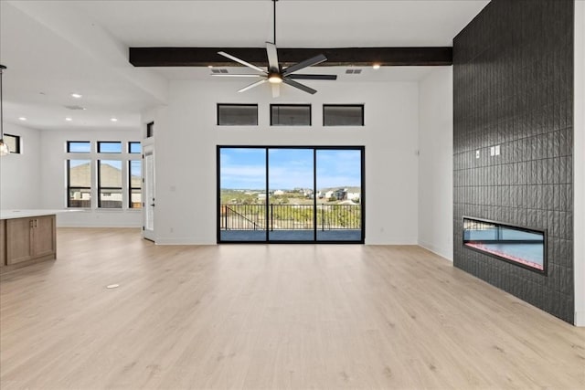 unfurnished living room with beamed ceiling, light wood-type flooring, a tile fireplace, and ceiling fan