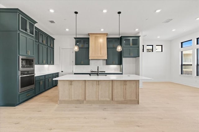 kitchen featuring light brown cabinets, an island with sink, stainless steel appliances, and light wood-type flooring