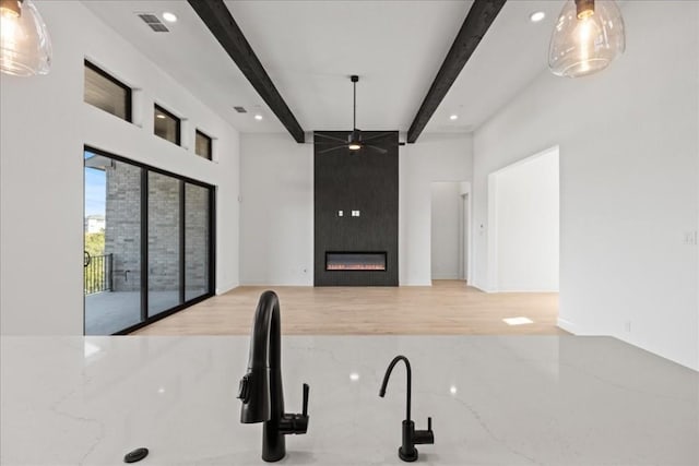 kitchen featuring ceiling fan, a fireplace, beamed ceiling, and wood-type flooring