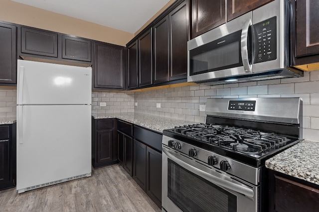 kitchen with stainless steel appliances, decorative backsplash, light stone countertops, dark brown cabinetry, and light hardwood / wood-style floors