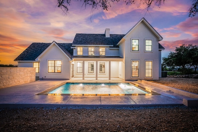 back house at dusk with pool water feature and a patio