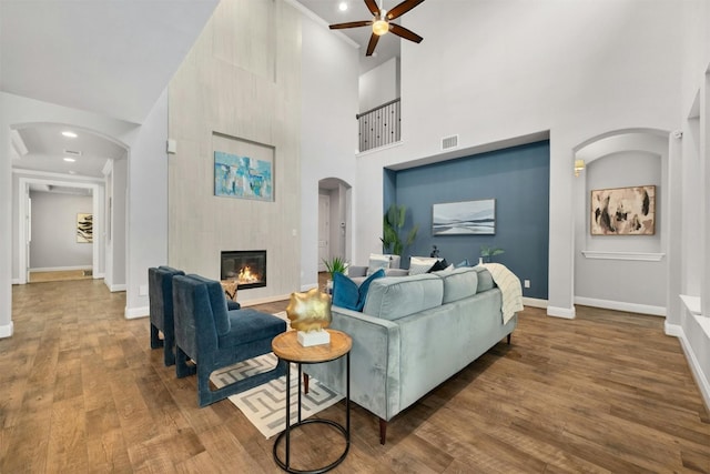 living room with hardwood / wood-style flooring, ceiling fan, a fireplace, and a towering ceiling