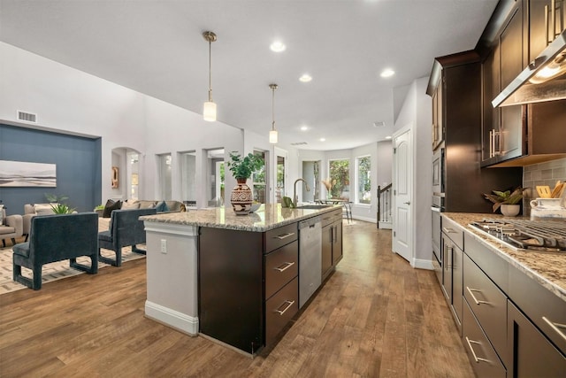 kitchen with dark brown cabinetry, a kitchen island with sink, range hood, and appliances with stainless steel finishes