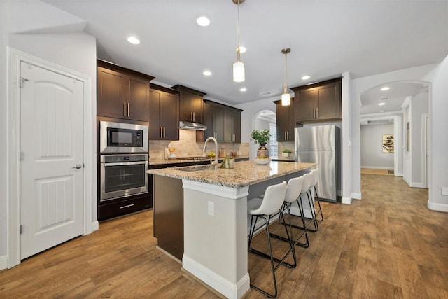 kitchen with sink, dark brown cabinets, a center island with sink, pendant lighting, and stainless steel appliances