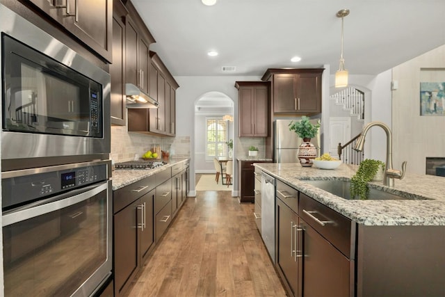 kitchen featuring sink, light wood-type flooring, appliances with stainless steel finishes, decorative light fixtures, and dark brown cabinets