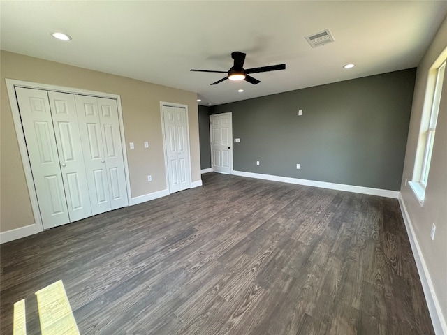 unfurnished bedroom with two closets, ceiling fan, and wood-type flooring