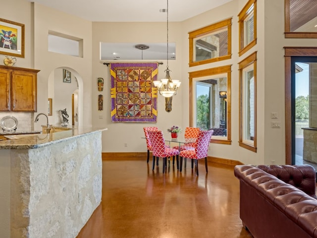 dining space featuring arched walkways, a high ceiling, baseboards, and a notable chandelier