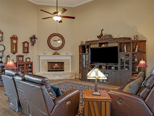 living room featuring hardwood / wood-style flooring, a stone fireplace, ornamental molding, and ceiling fan