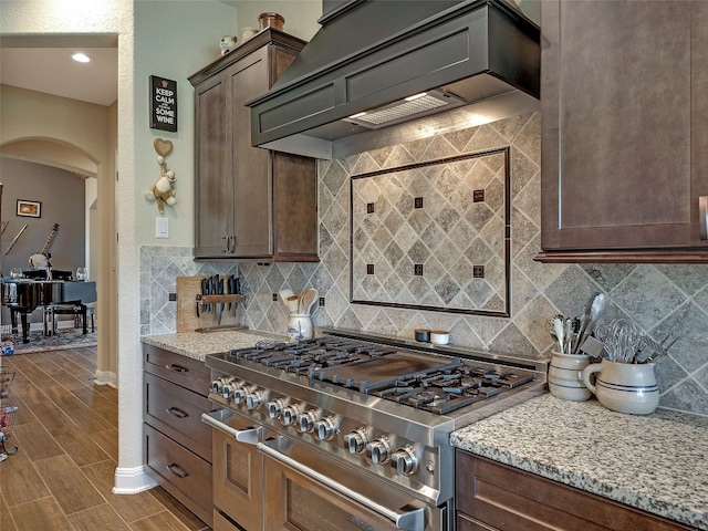 kitchen featuring double oven range, light stone counters, custom exhaust hood, and decorative backsplash