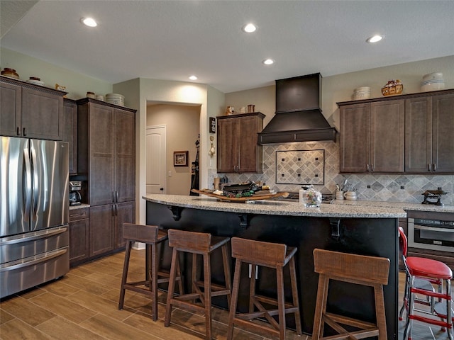 kitchen featuring decorative backsplash, custom exhaust hood, appliances with stainless steel finishes, light wood-type flooring, and a kitchen island