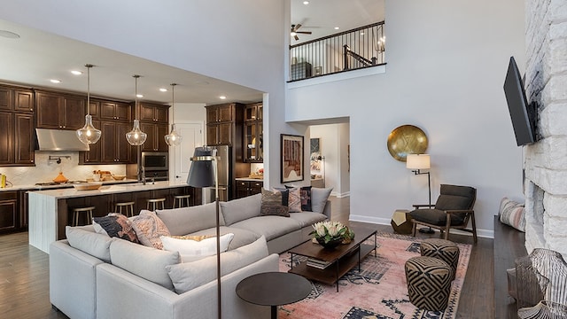 living room featuring ceiling fan, a stone fireplace, dark hardwood / wood-style flooring, and a towering ceiling