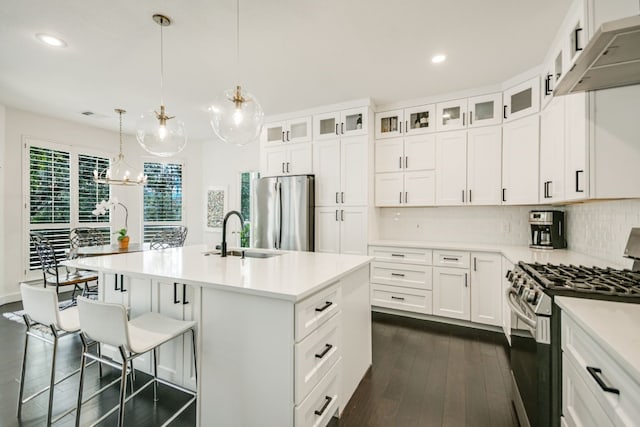 kitchen featuring pendant lighting, sink, appliances with stainless steel finishes, white cabinetry, and a center island with sink