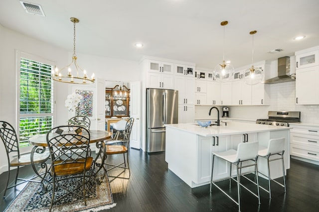 kitchen featuring white cabinetry, sink, wall chimney range hood, stainless steel appliances, and a center island with sink