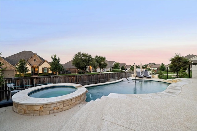 pool at dusk with a patio, pool water feature, and an in ground hot tub