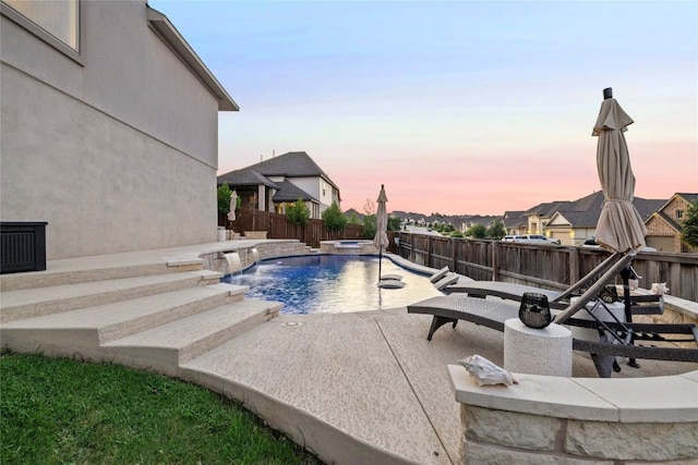 pool at dusk with pool water feature, an in ground hot tub, and a patio area