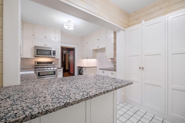 kitchen featuring appliances with stainless steel finishes, white cabinets, and light stone counters