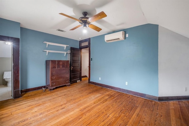 unfurnished bedroom with a wall mounted AC, wood-type flooring, visible vents, and baseboards