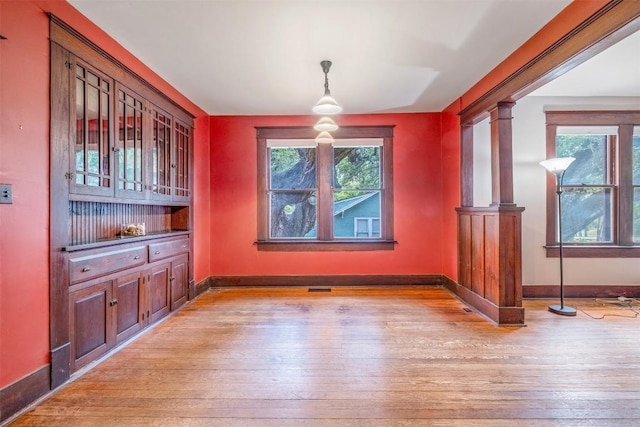 unfurnished dining area featuring ornate columns, visible vents, light wood-style flooring, and baseboards